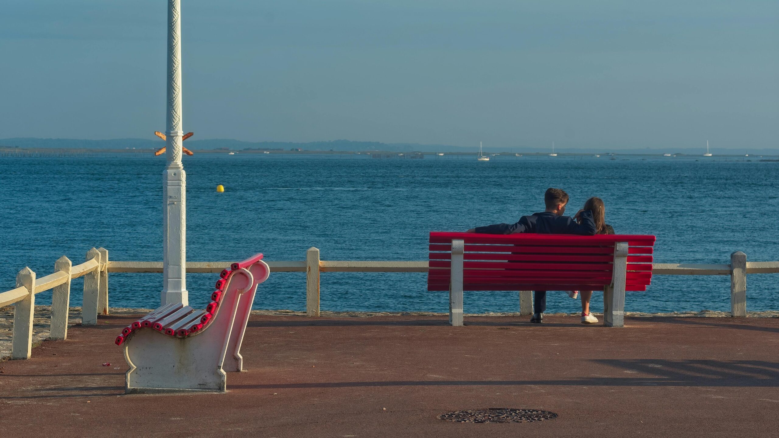 A couple enjoying a quiet moment on a red bench by the Arcachon sea.